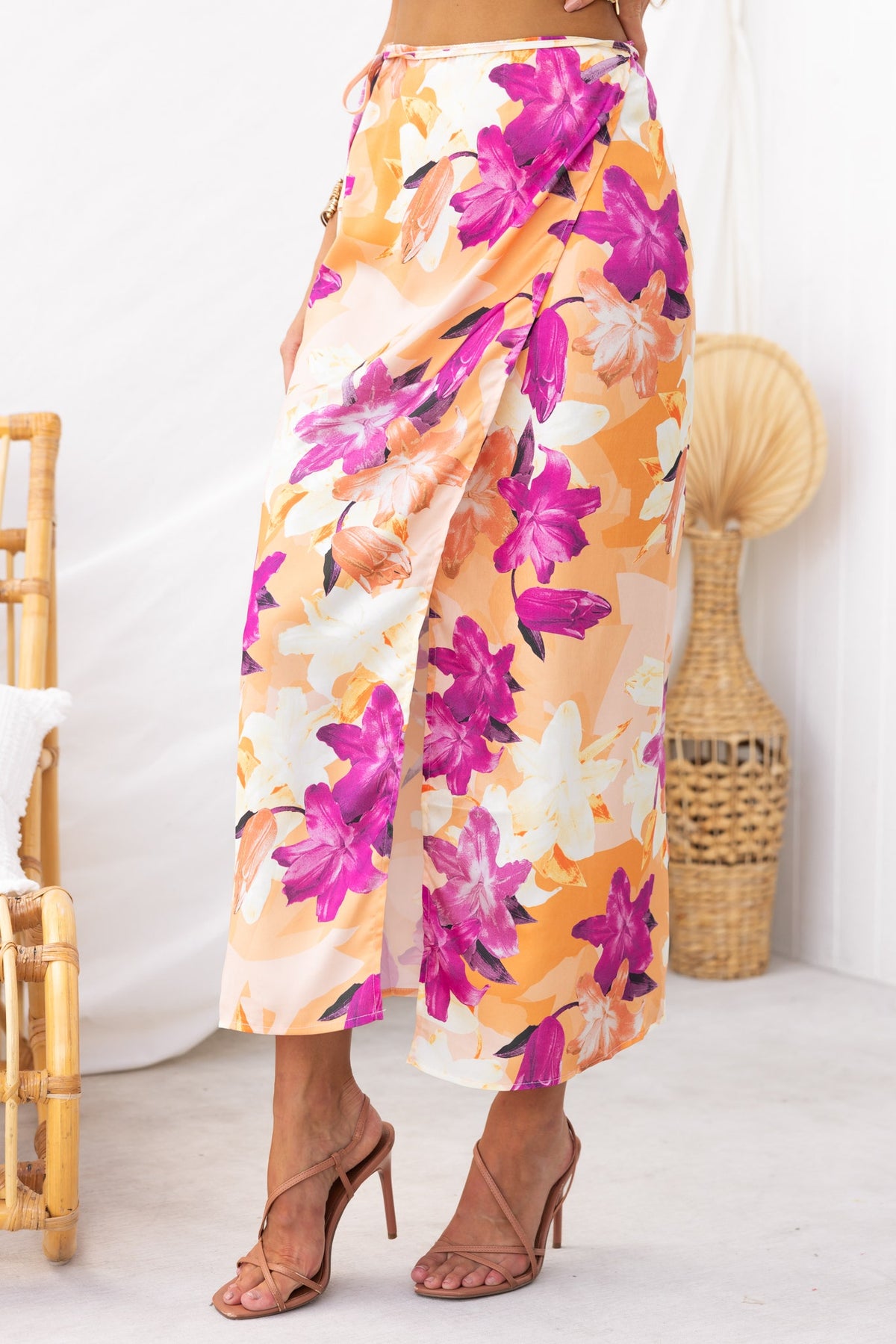 Nerida Wrap Midi Skirt featuring vibrant floral print, asymmetric hem, and satin finish, styled with heels.