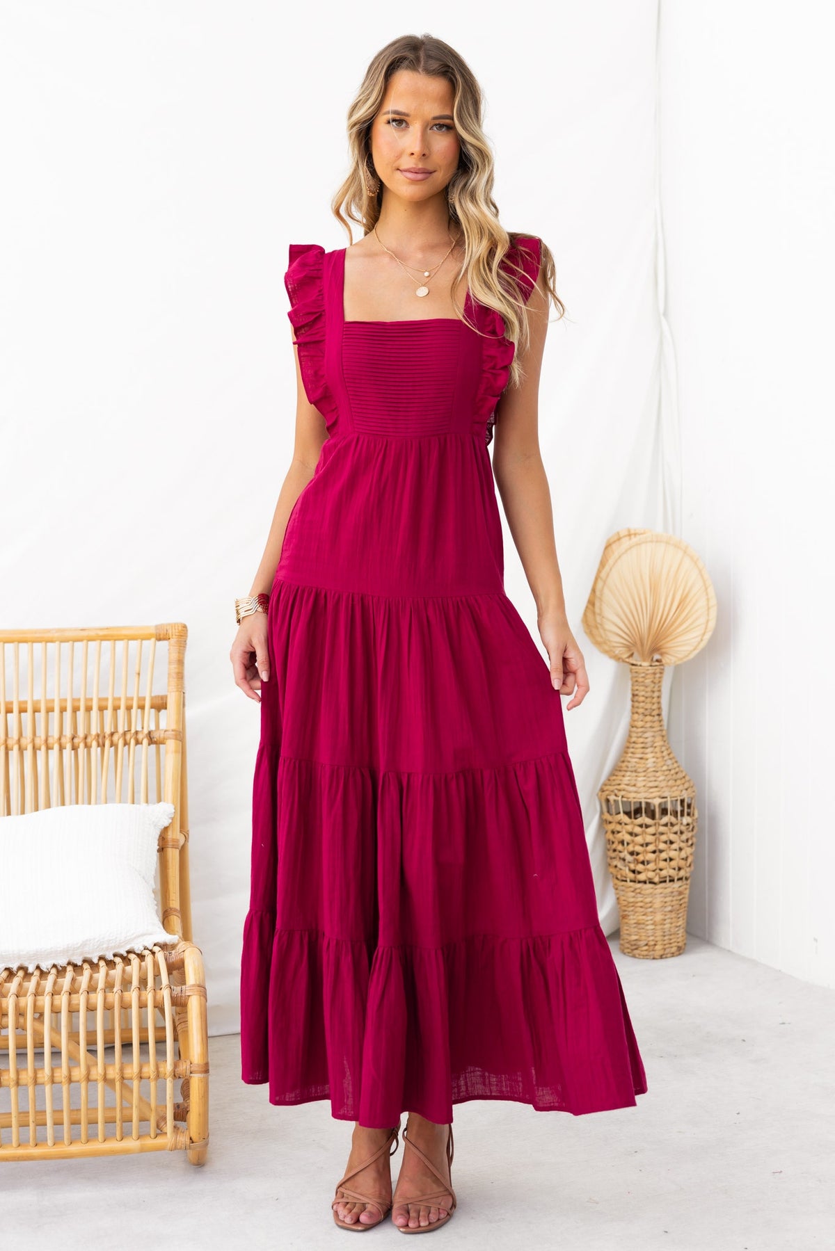 Model wearing Giada Maxi Dress in fuchsia with ruffled sleeves and tiered skirt, styled in a bright indoor setting.