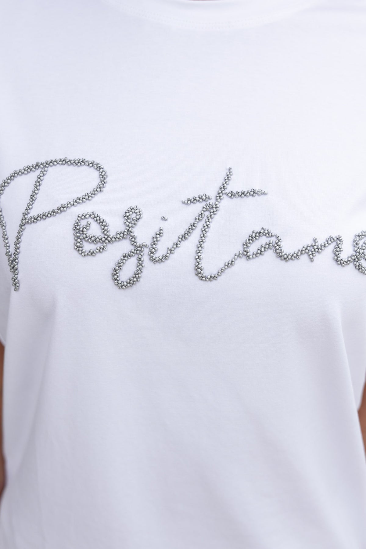 Close-up of the Landon Tee featuring 'Positano' in bead detail on a soft white cotton fabric.