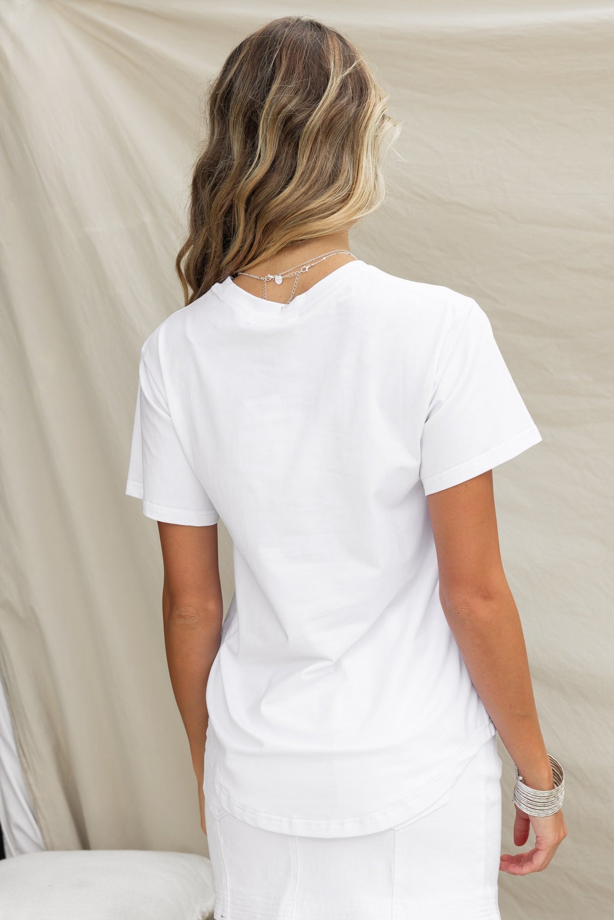 Woman wearing the Landon Tee, a white cotton shirt with a round neckline and relaxed fit, shown from the back.