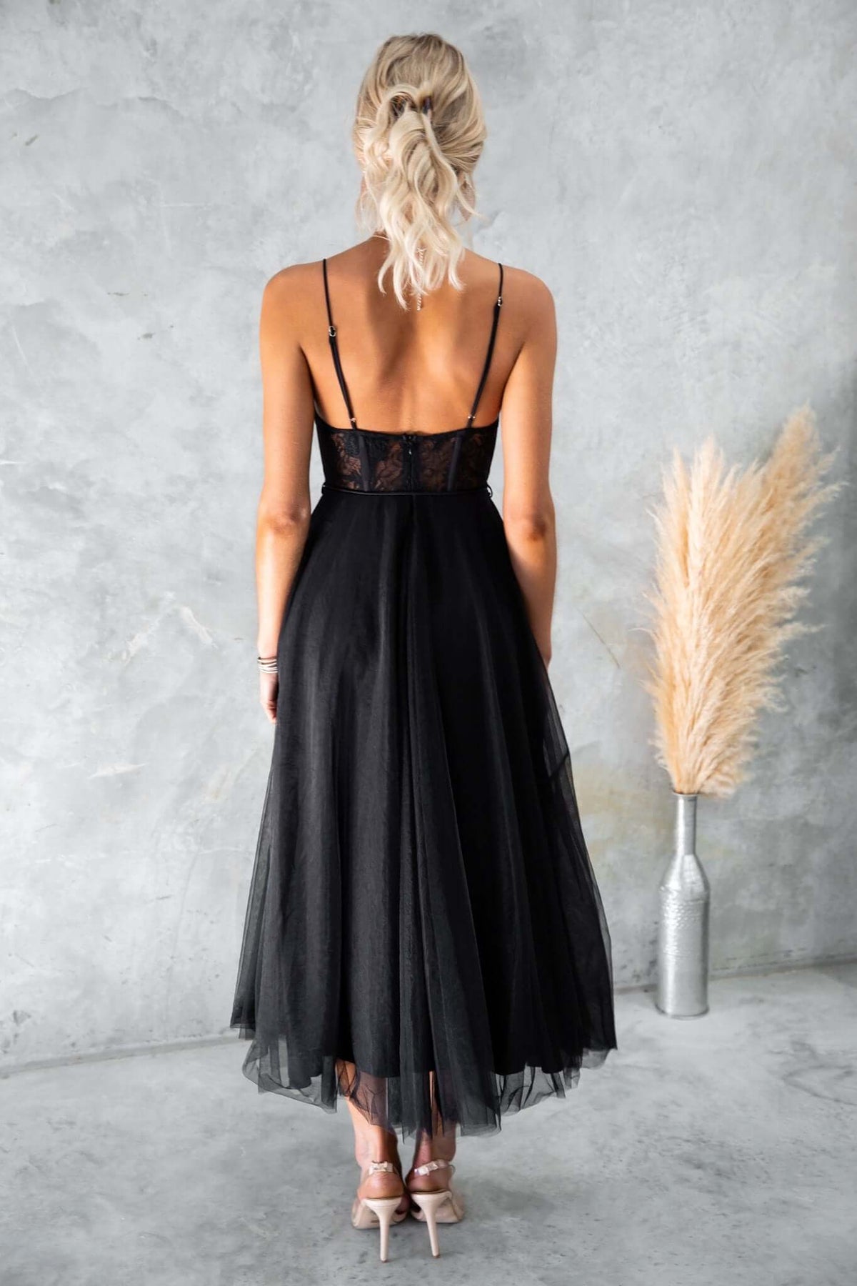 Model wearing a black tulle maxi dress with adjustable straps and lace detail, viewed from the back.