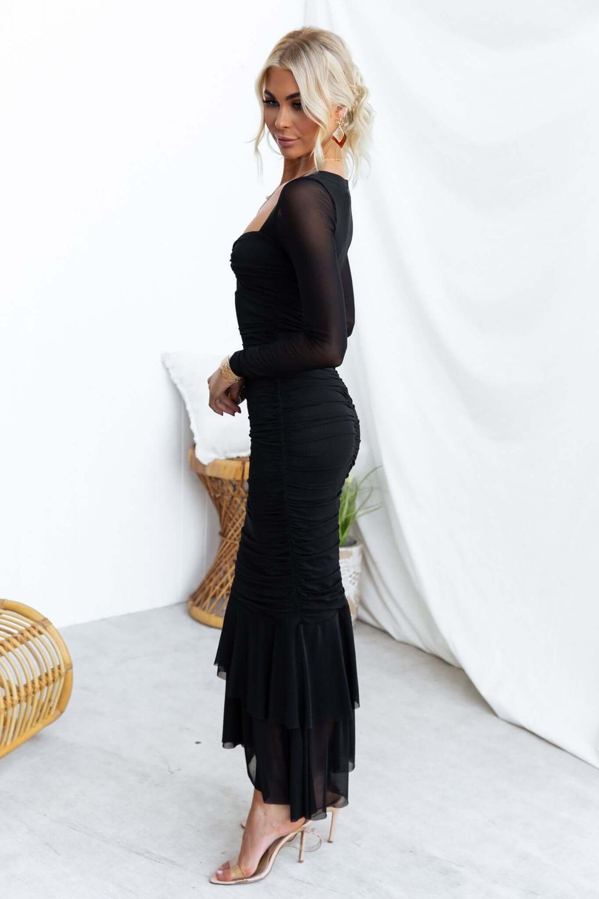 Zhari Maxi Dress in black with twist detail, cut-out bust, and mesh overlay, modeled by a woman in a stylish setting.