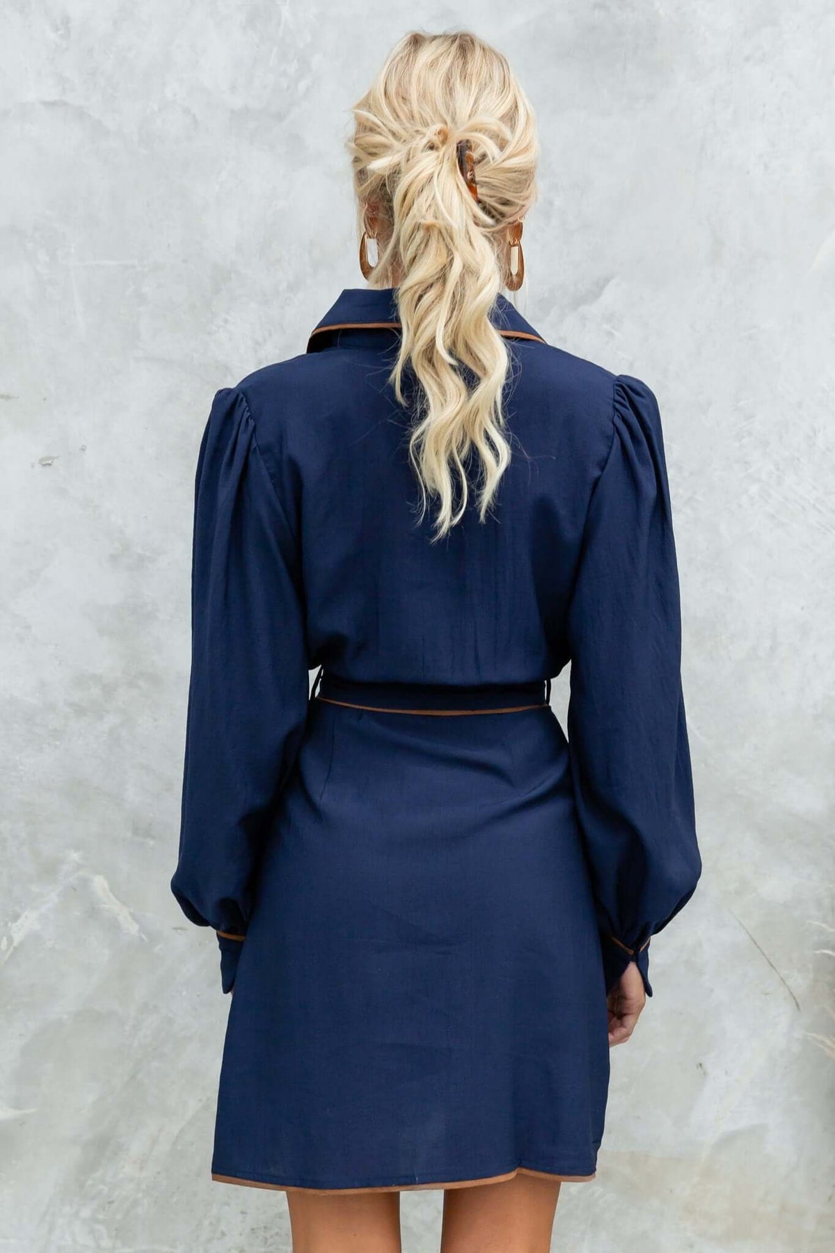 Back view of the Pianolo Dress in navy with puff sleeves and removable tie, styled with loose hair and a chic look.