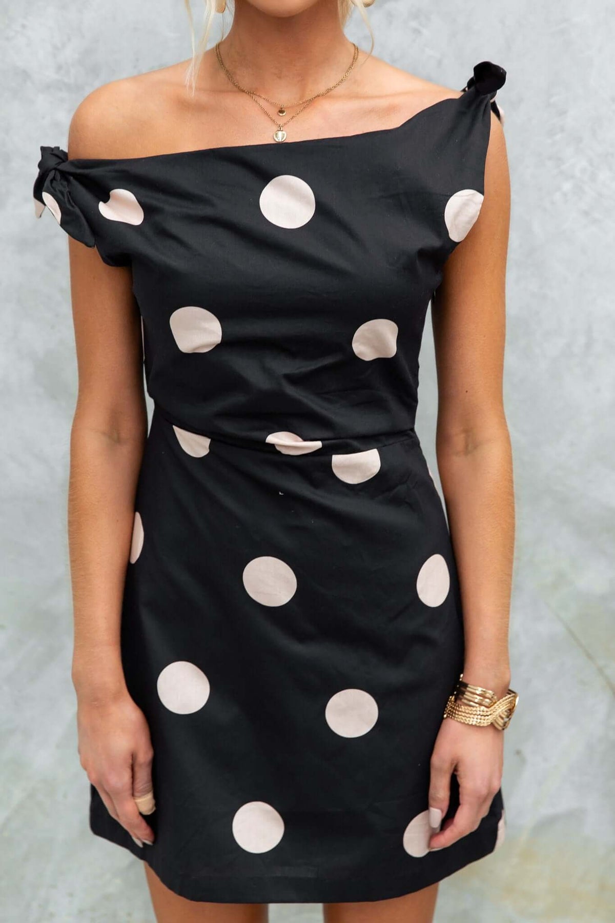 Model wearing the Roberta dress featuring black fabric with polka dots, asymmetric neckline, and tie straps.