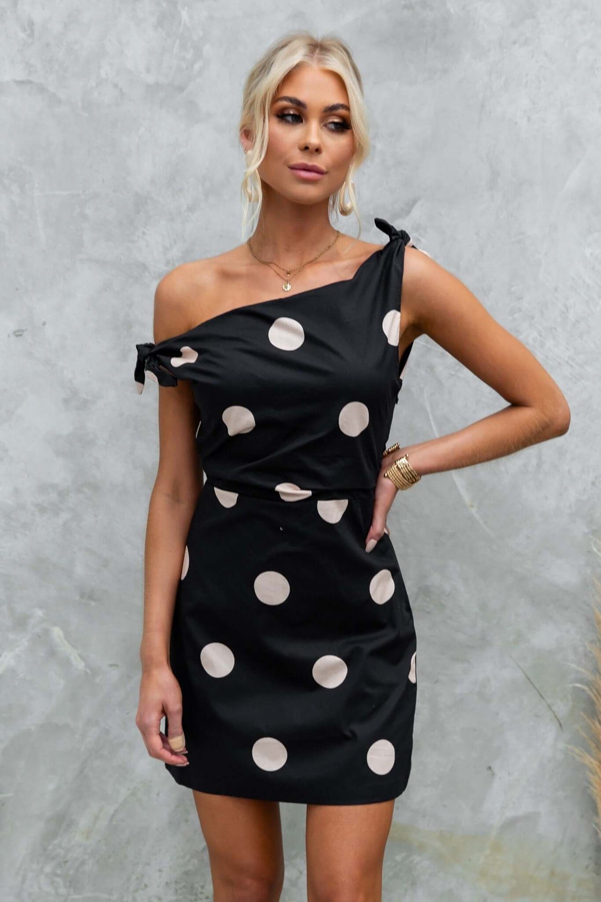 Model wearing a black Roberta Dress with polka dots, featuring an asymmetric neckline and tie straps.