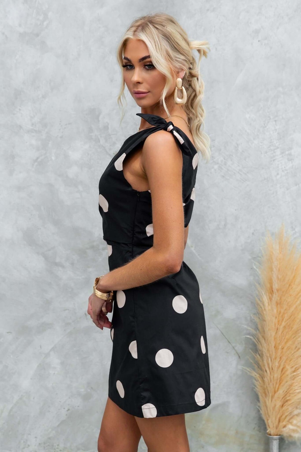 Side view of a model in a chic black polka dot dress with tie straps, showcasing elegant style and modern design.