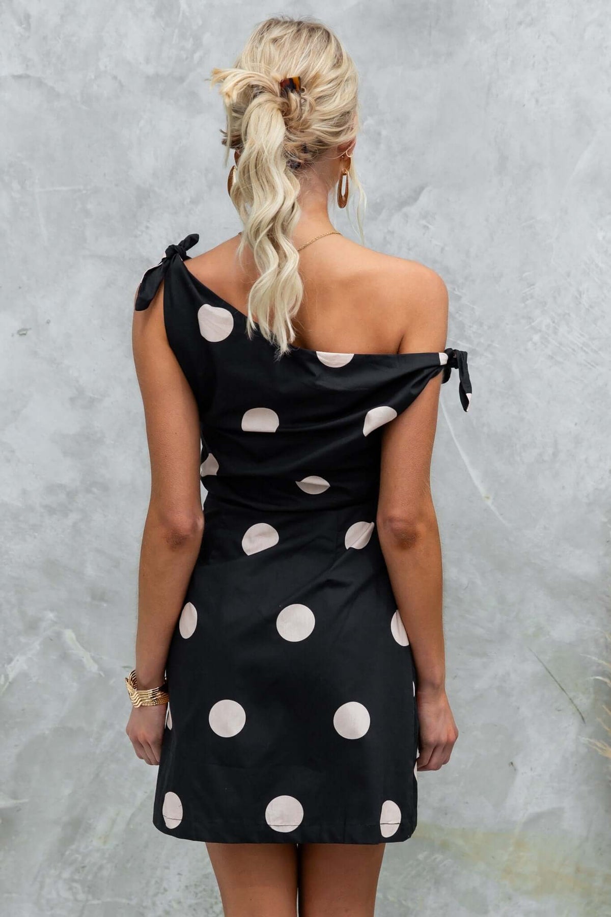 Back view of black polka dot Roberta Dress with asymmetric neckline and tie straps.