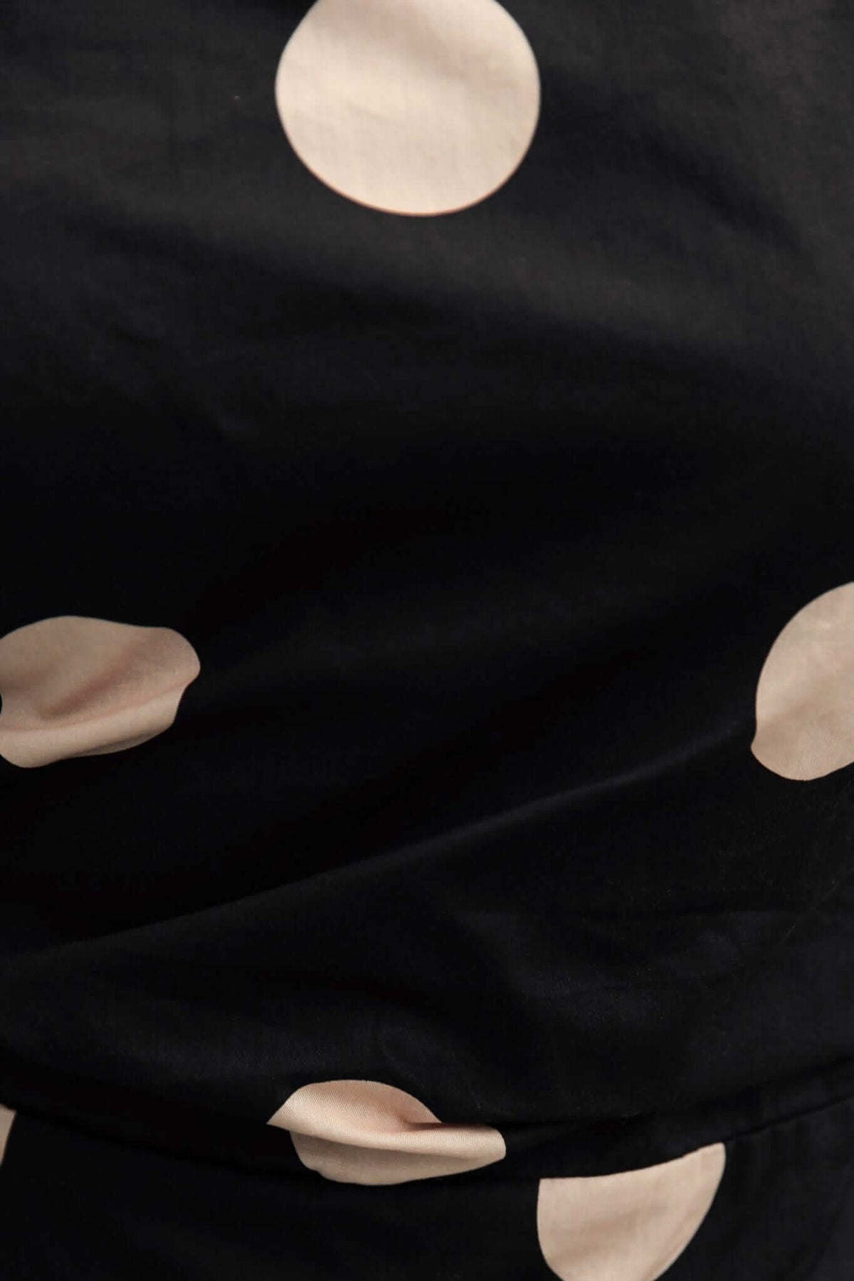 Close-up of black fabric featuring large beige polka dots, showcasing texture and design of the Roberta Dress.