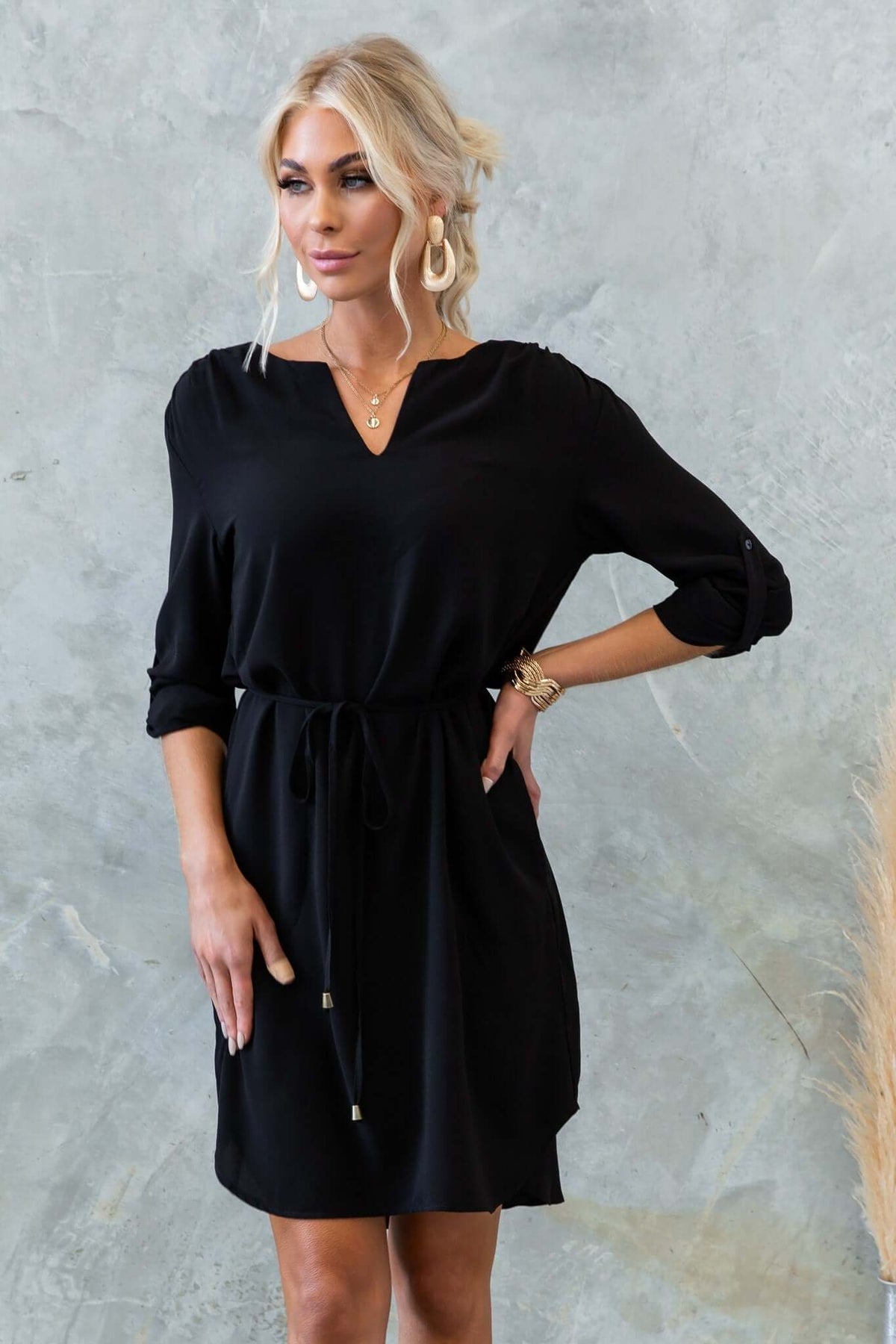 Model wearing the Deklyn Dress, a chic black dress with a V-neckline and adjustable tie at the waist.