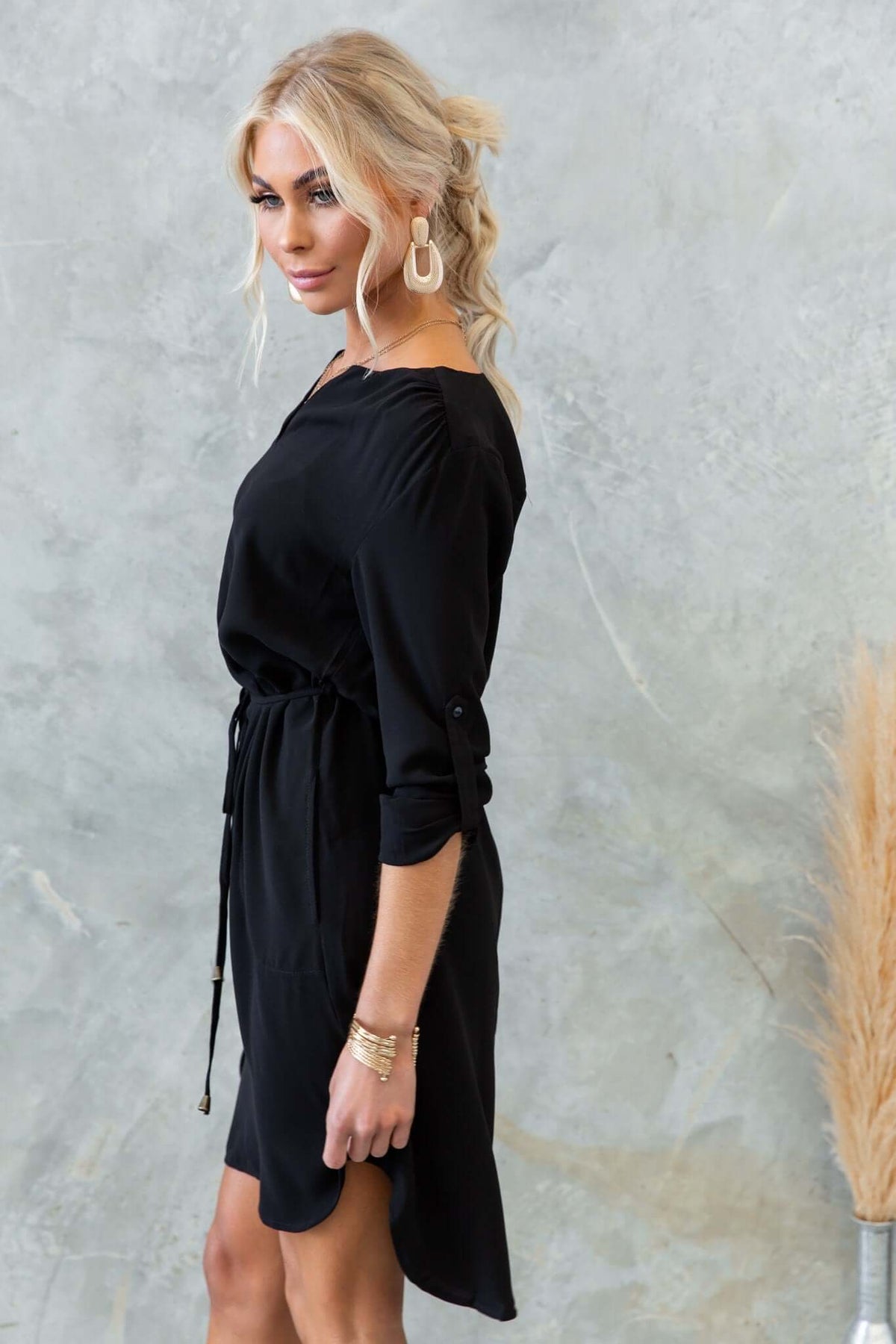 Side view of the Deklyn Dress in black with a V-neckline, removable tie, and pockets, on a model.
