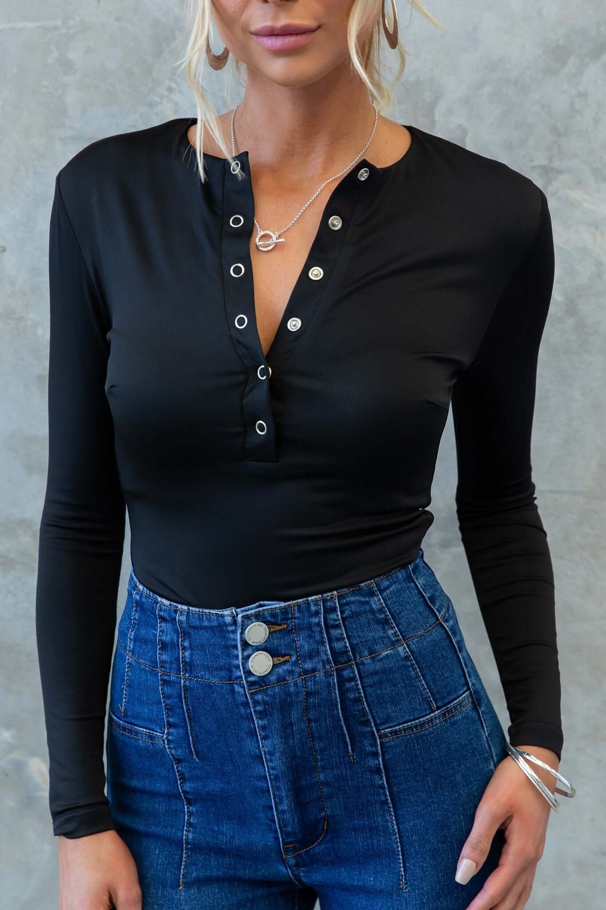 Model wearing the Unfair Bodysuit in black with button-up closure, paired with high-waisted denim jeans.