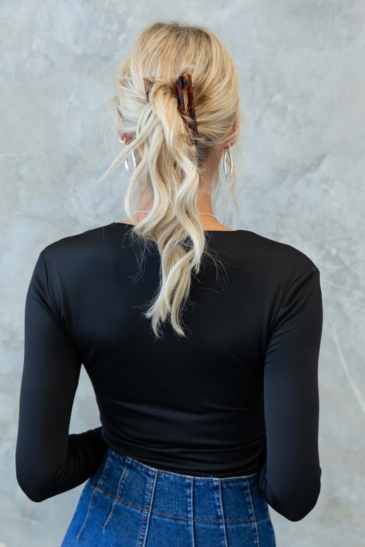 Back view of a blonde woman in a black bodysuit styled with a hair clip, paired with a high-waisted denim skirt.
