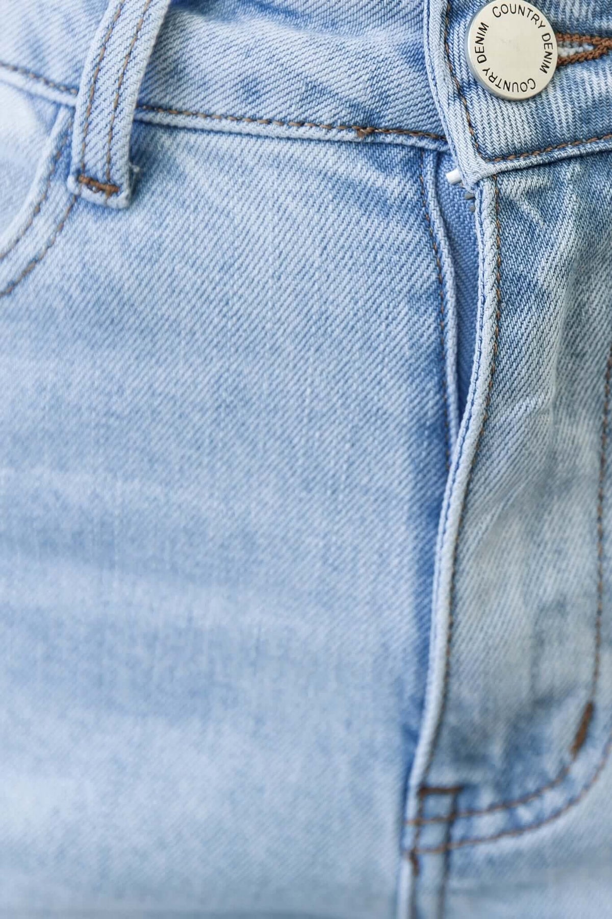 Close-up of Amber Jeans showcasing mid-high waist fit, button detail, and light blue distressed denim texture.