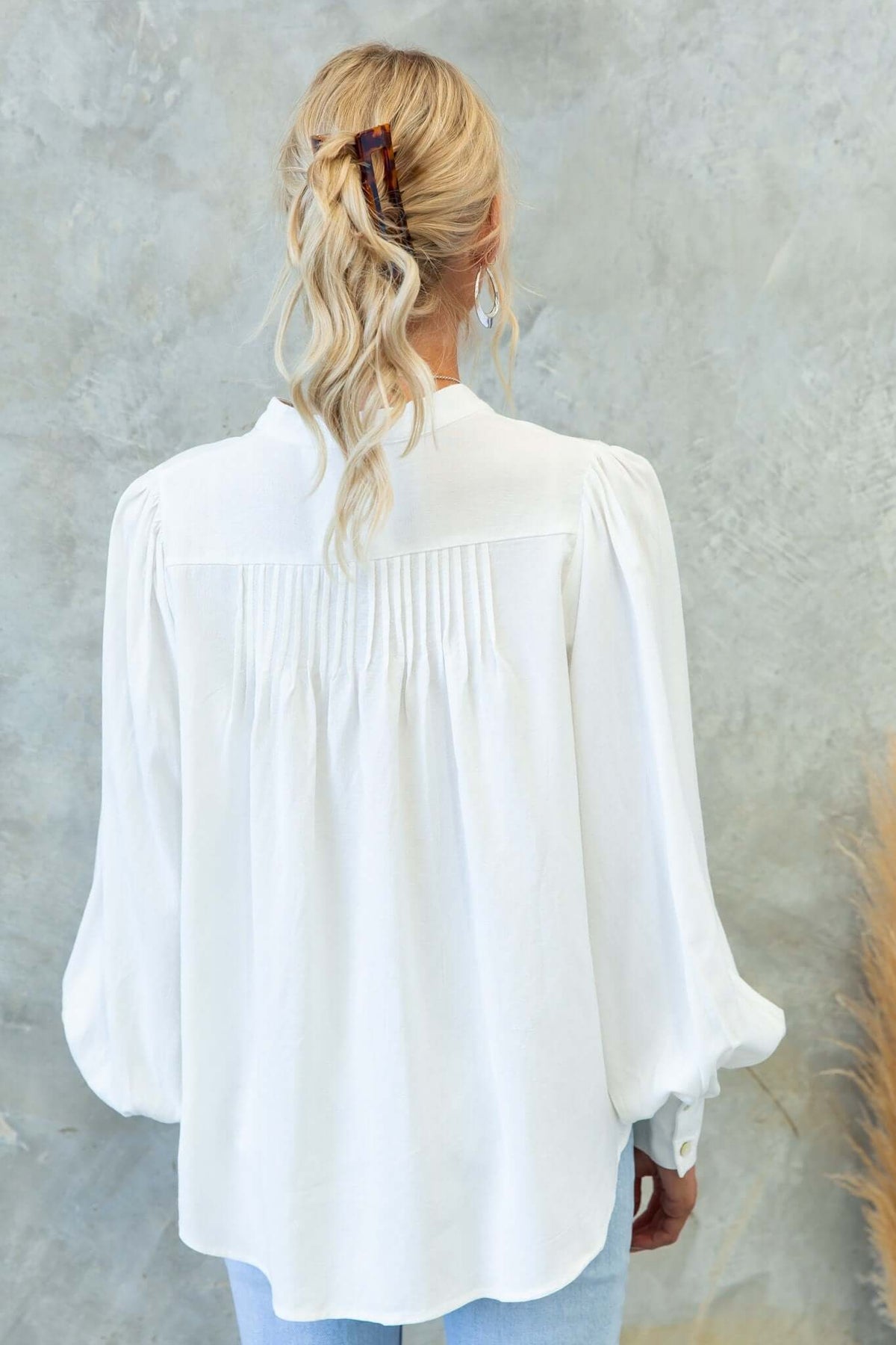 Back view of a Brunie Shirt in white with puffed sleeves and pleated detailing, styled casually with light blue jeans.