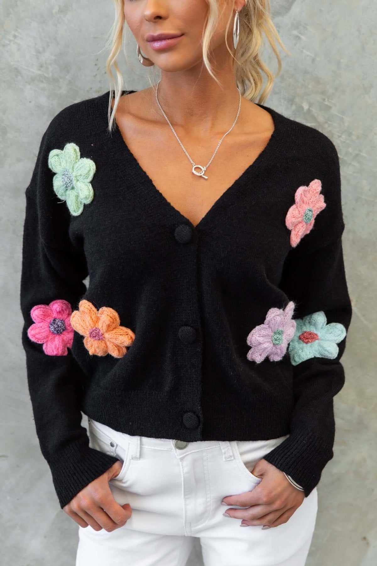 Black Varian Cardigan with colorful flower embroidery, V-neckline, and button-up front, styled with white jeans.