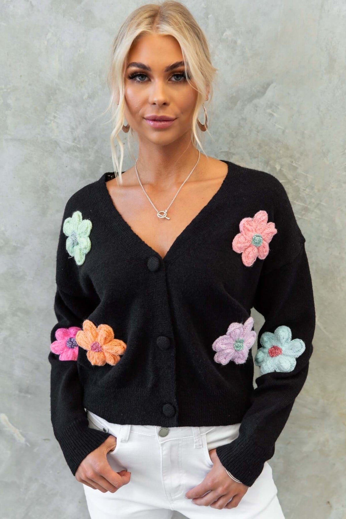 Black Varian cardigan with floral appliques, V-neckline, and button-up front, worn with white jeans.