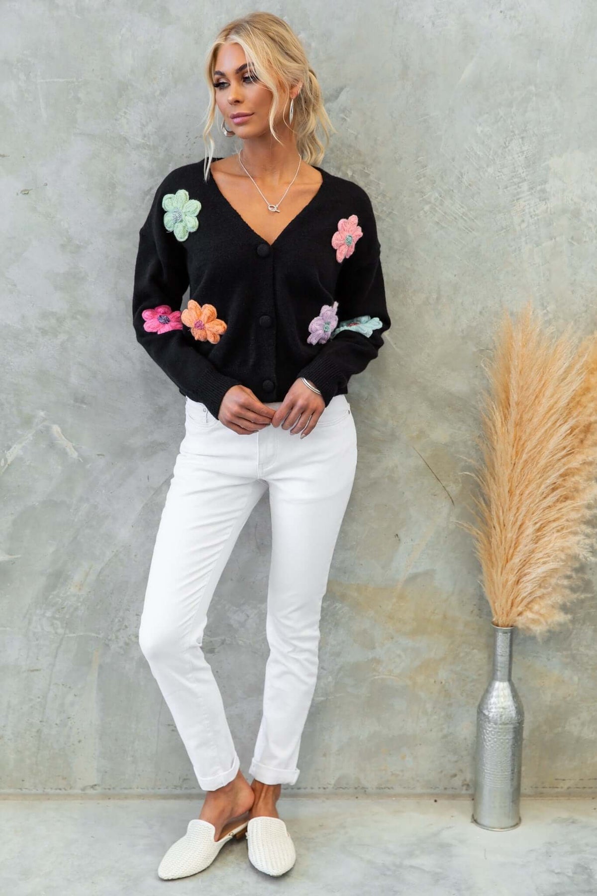 Model wearing a black Varian cardigan with floral embellishments, paired with white pants and soft slippers.