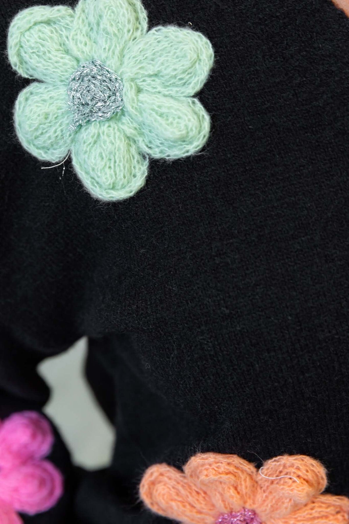 Close-up of black cardigan with colorful knitted flower appliques in mint green, orange, and pink.