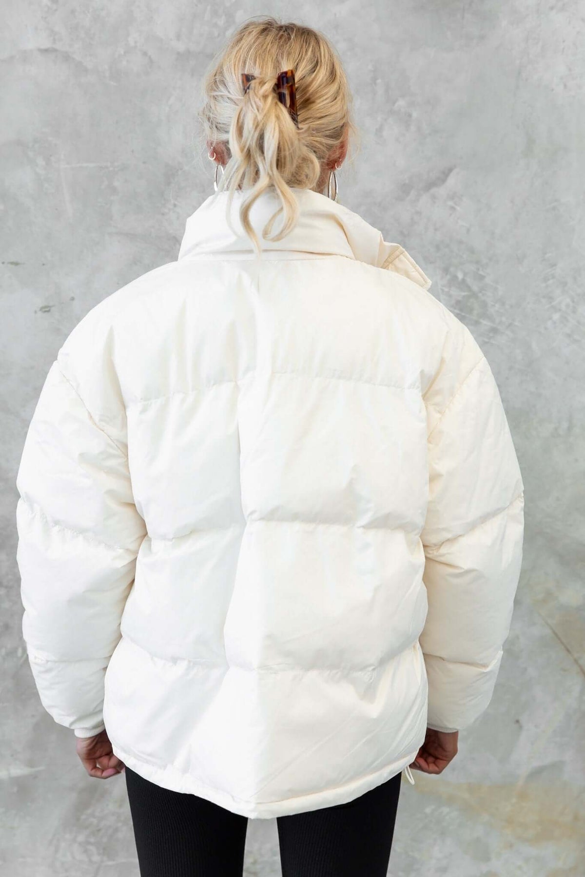 Back view of a woman in a white Cooper Puffer Jacket with a high neckline and padded design.