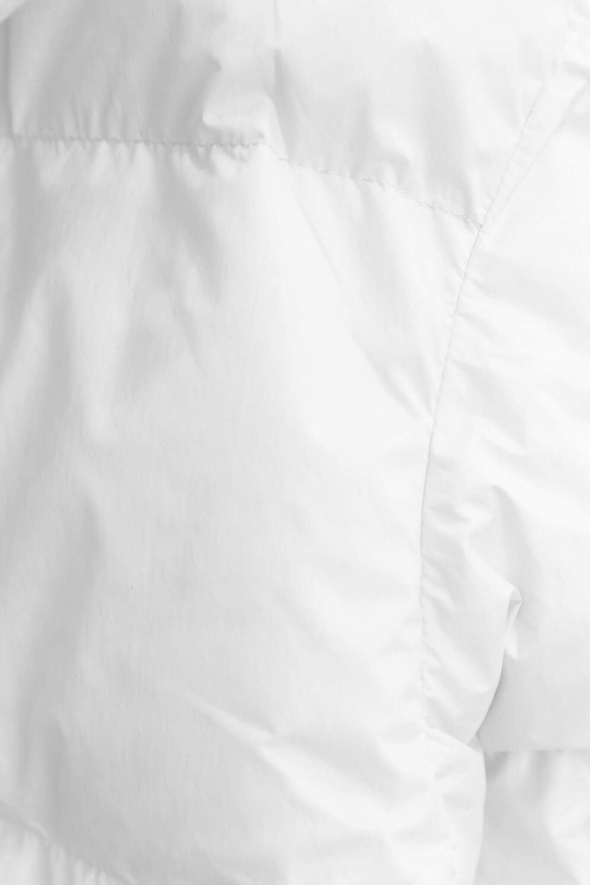 Close-up of the Avril Puffer Jacket's white fabric texture, showcasing its soft, insulated design and durable stitching.