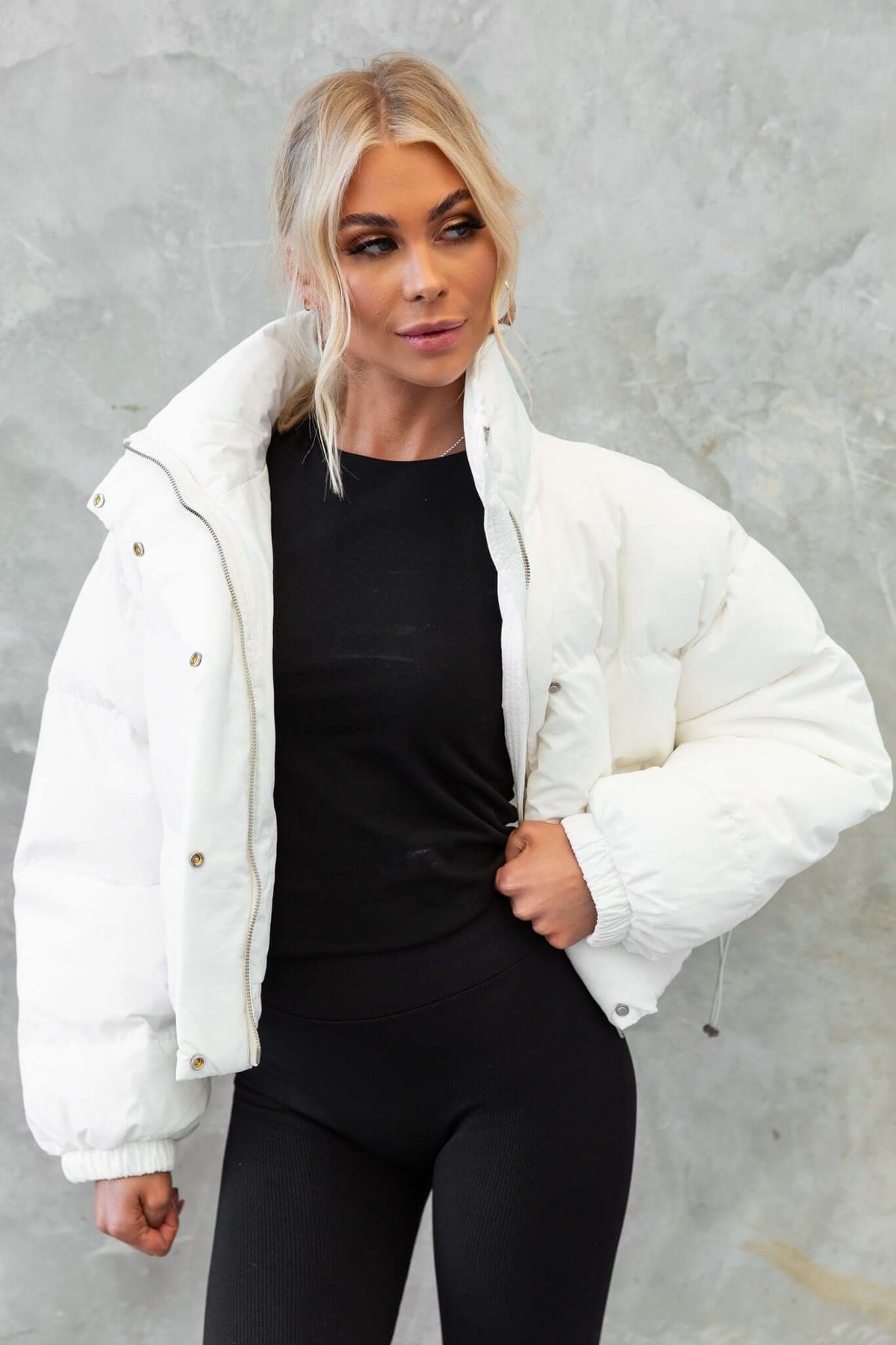 Woman wearing white Avril Puffer Jacket with high neckline and button closure, styled with black outfit.