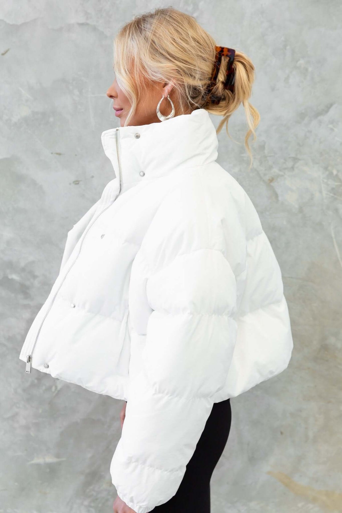 Model wearing a white Avril Puffer Jacket with high neckline and elastic cuffs, styled elegantly against a textured backdrop.