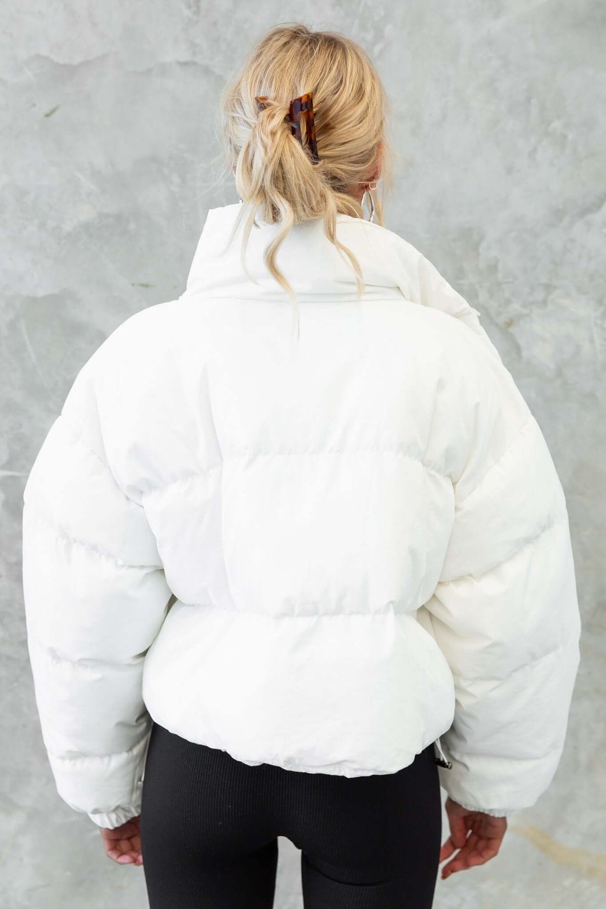Back view of a white Avril puffer jacket with high neckline and elastic cuffs, paired with black leggings.