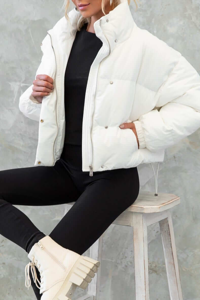 Model wearing white Avril Puffer Jacket, featuring high neckline, zip closure, and elastic cuffs, styled with leggings and boots.