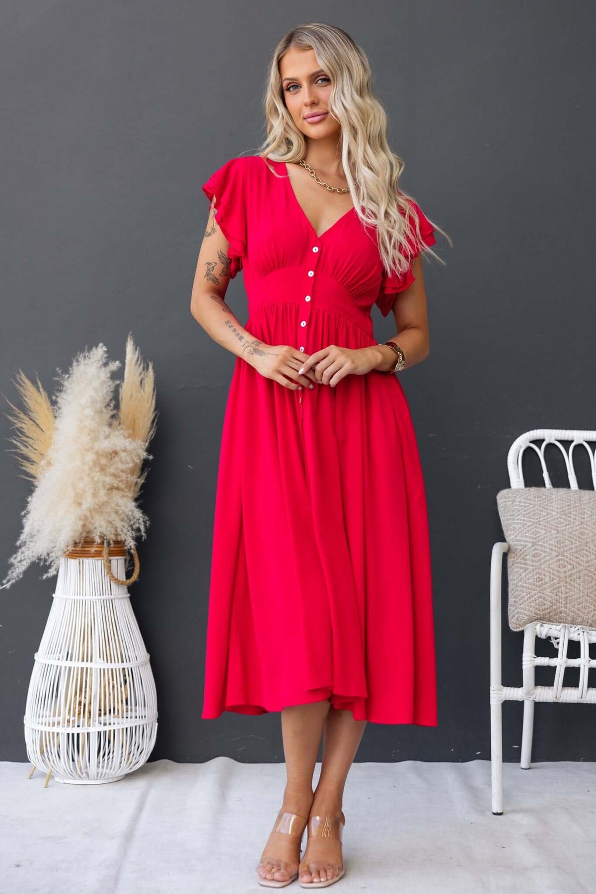 Model wearing Joelle Midi Dress in vibrant red, featuring a button-up front and flowing skirt, styled with natural background.