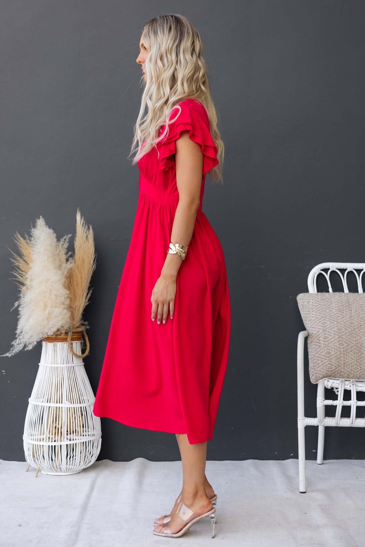 Side view of a woman wearing a red Joelle Midi Dress with ruffle sleeves and a flowy silhouette.