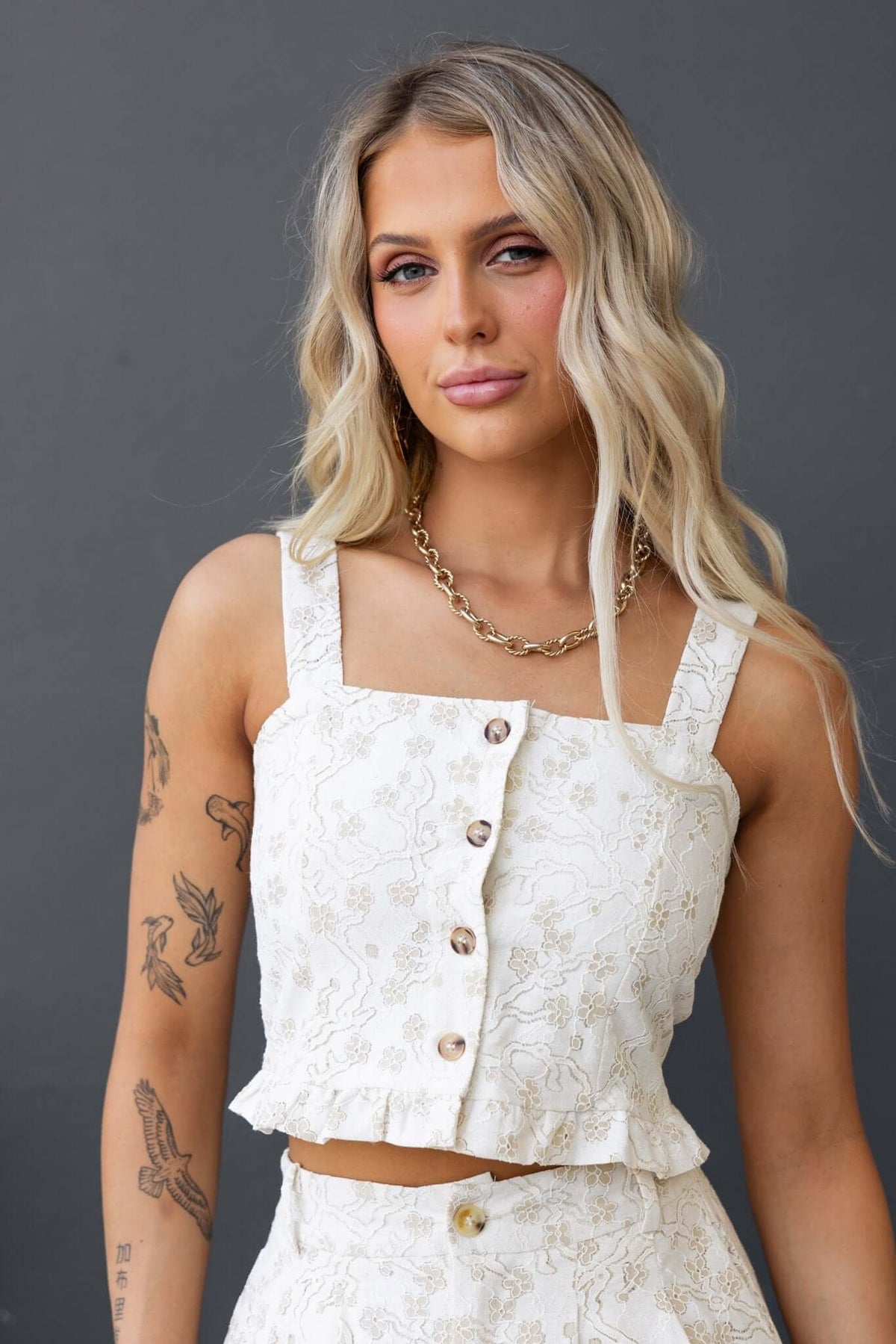 Ella Top featuring adjustable straps, button-up front, and a stylish ruffled hem, modeled by a woman with long blonde hair.