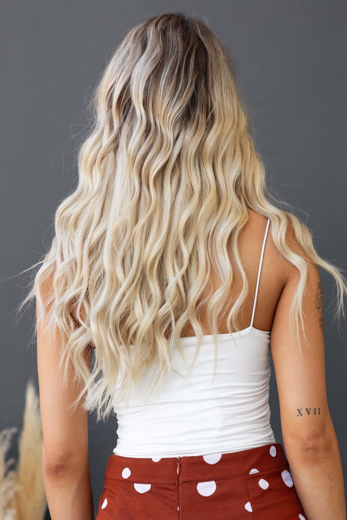 Back view of a woman wearing a white spaghetti strap bodysuit with wavy blonde hair.