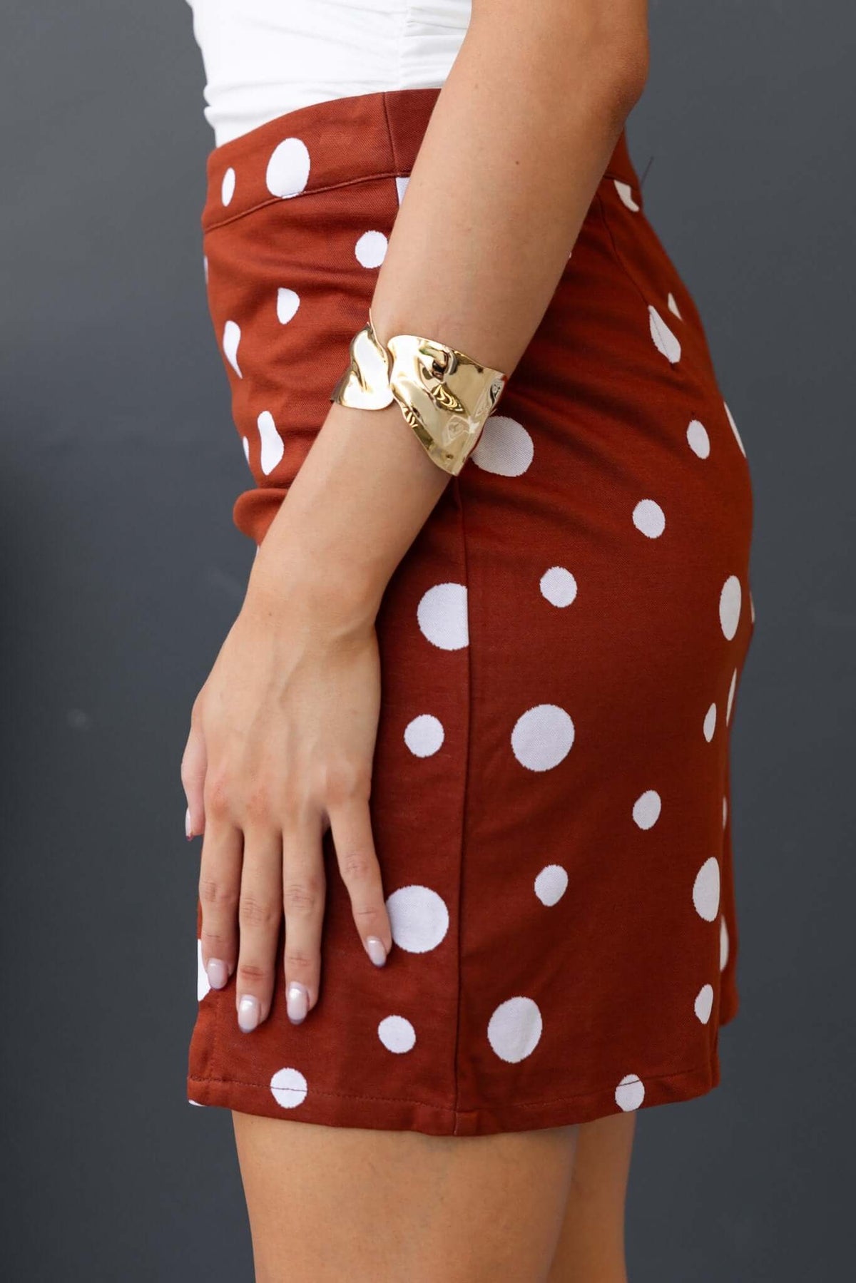 Side view of the Gelida Skirt featuring a mid-high waist and brown fabric with white polka dots.
