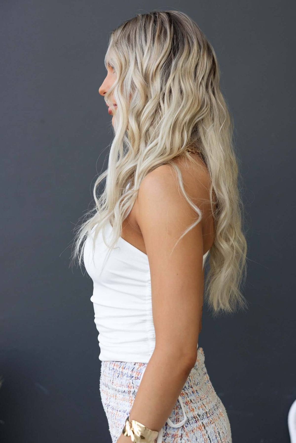 Side view of a woman wearing a white one-shoulder top with a twist strap, showcasing soft waves in her hair.