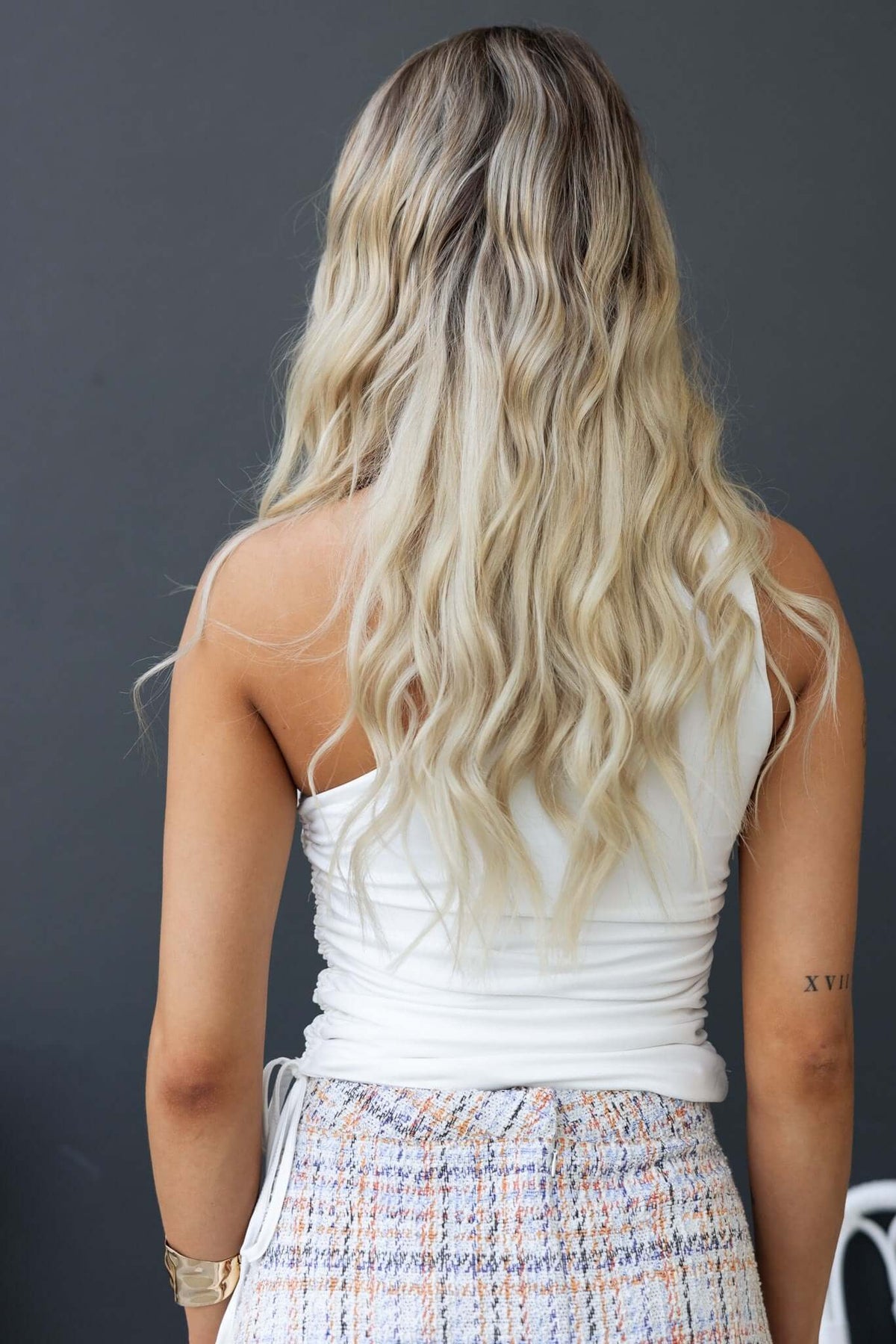 Back view of model wearing Dottie Top, showing one-shoulder design and wavy hair.