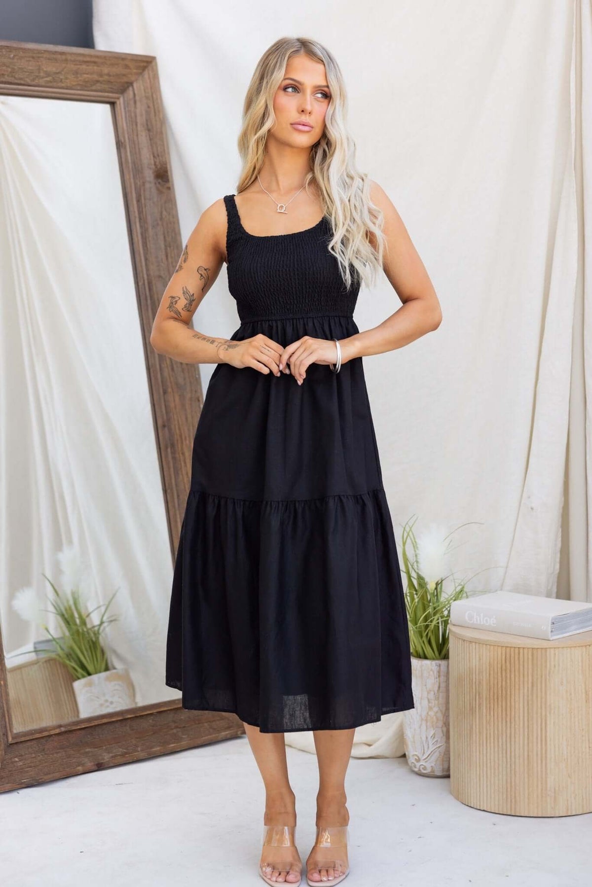 Model wearing a black Haidy Midi Dress featuring an elastic bodice, pockets, and a tiered hem.