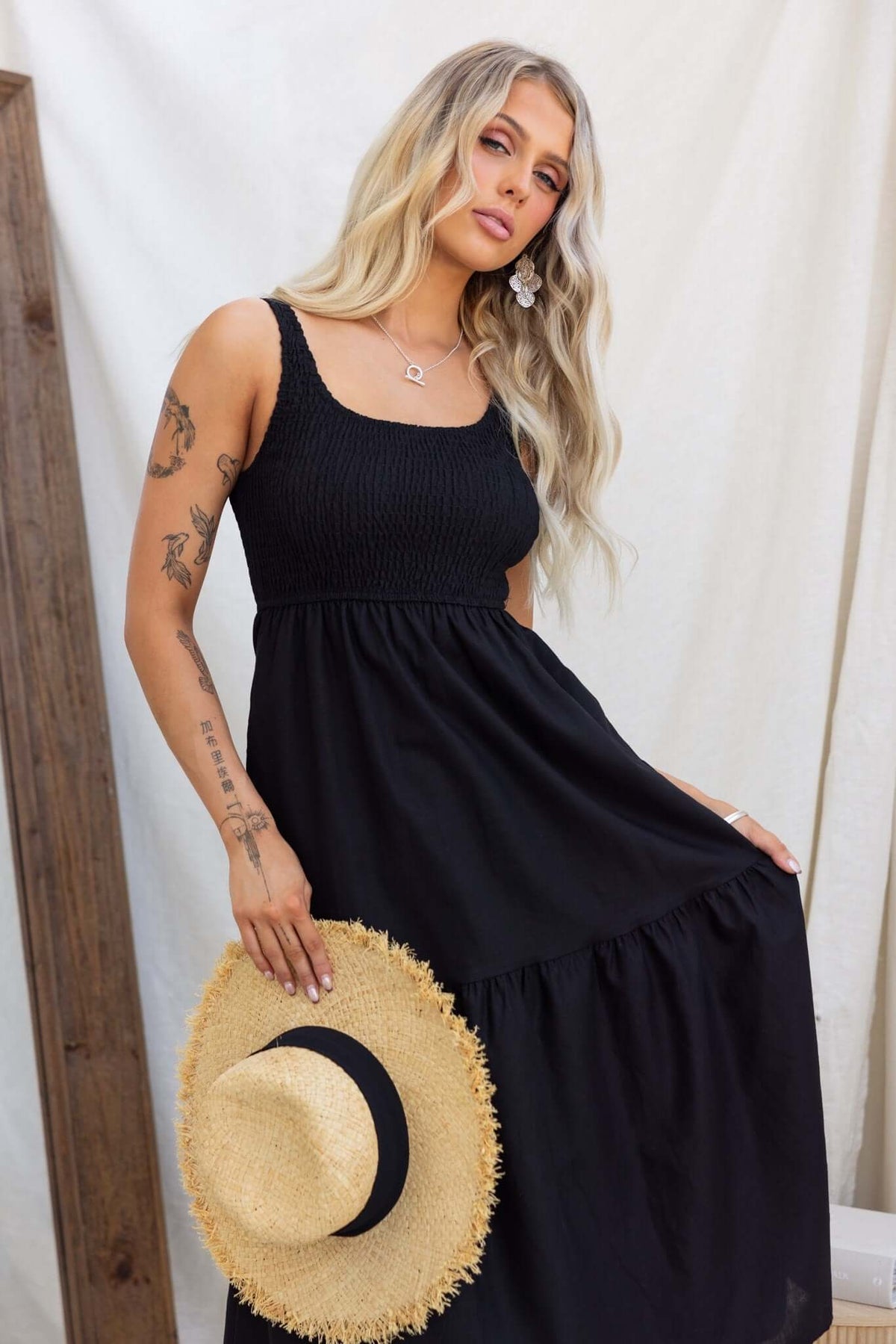 Model wearing Haidy Midi Dress in black, featuring elastic bodice and pockets, styled with a straw hat.