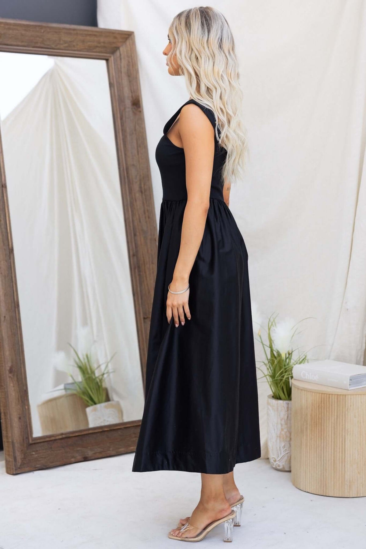 Flint Maxi Dress in black, featuring a jersey bodice, side pockets, and a flowing skirt, styled with clear heels.
