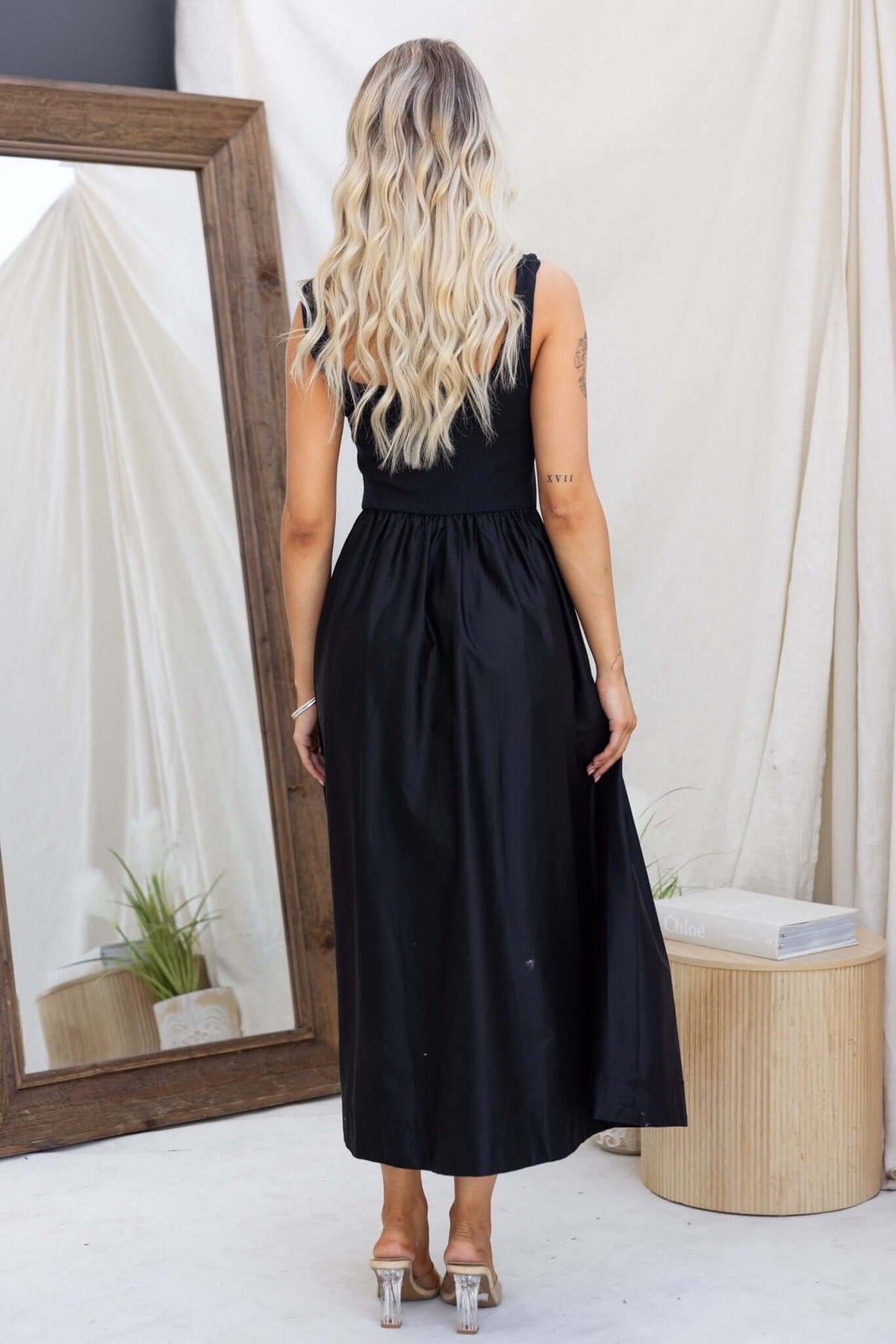 Back view of a woman in a black Flint Maxi Dress featuring a jersey bodice and flowing skirt, styled with long hair.