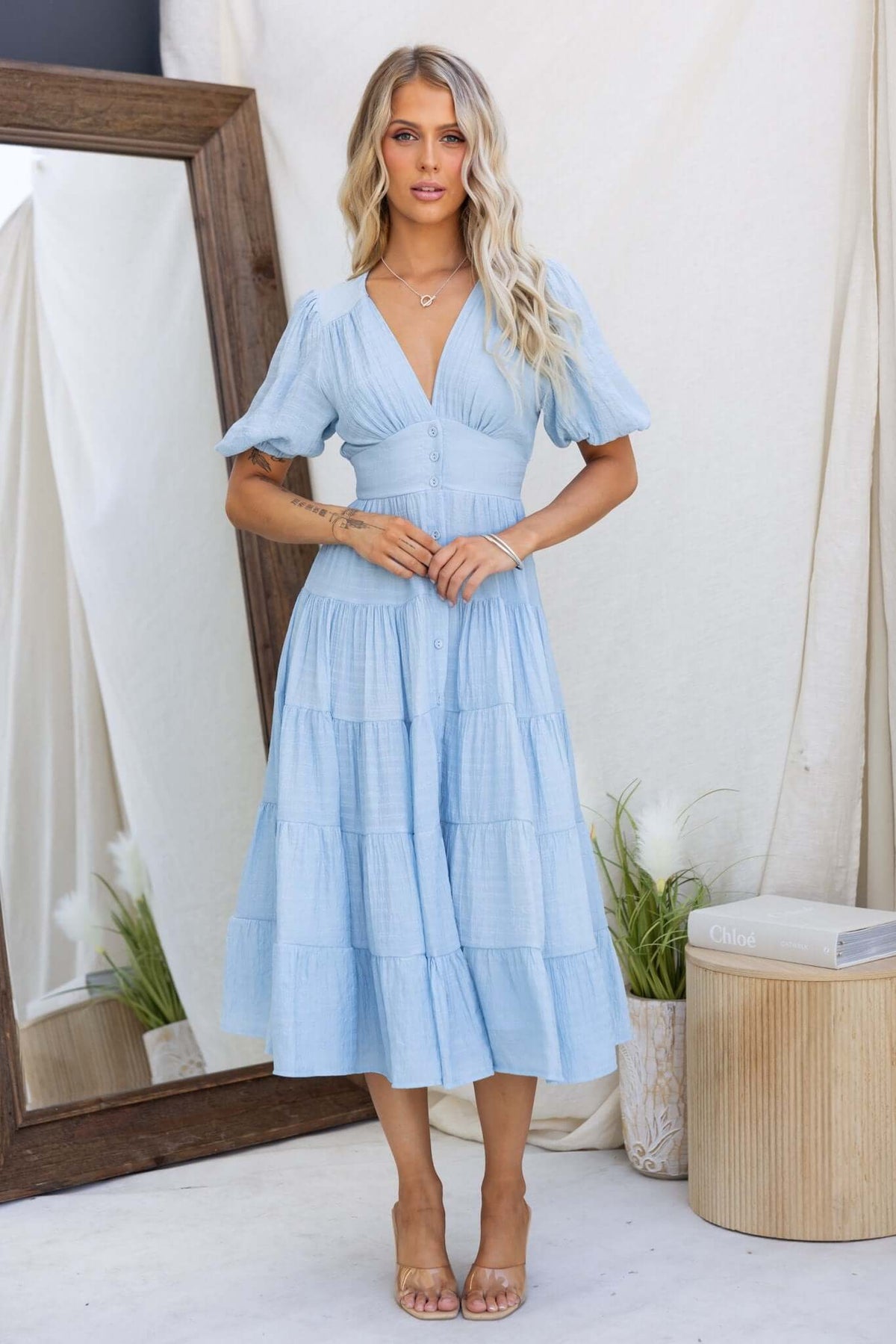 Light blue midi dress with V-neckline and button-up front, featuring puff sleeves and a tiered skirt, perfect for summer events.