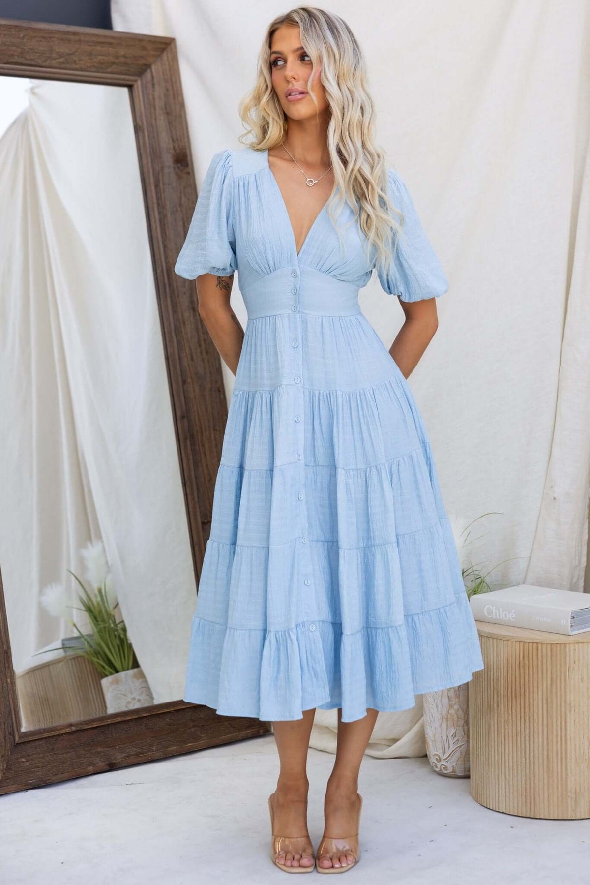 Light blue Bindi Midi Dress with V-neckline, button-up front, and tiered skirt, styled with strappy heels.