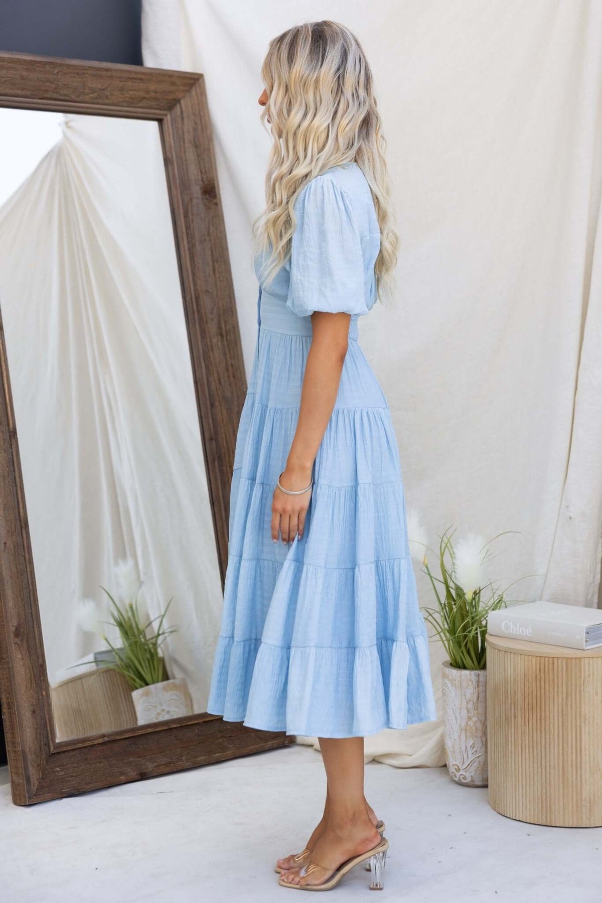 Elegant blue Bindi midi dress showcasing a V-neckline, button-up front, and tiered skirt, modeled by a woman.