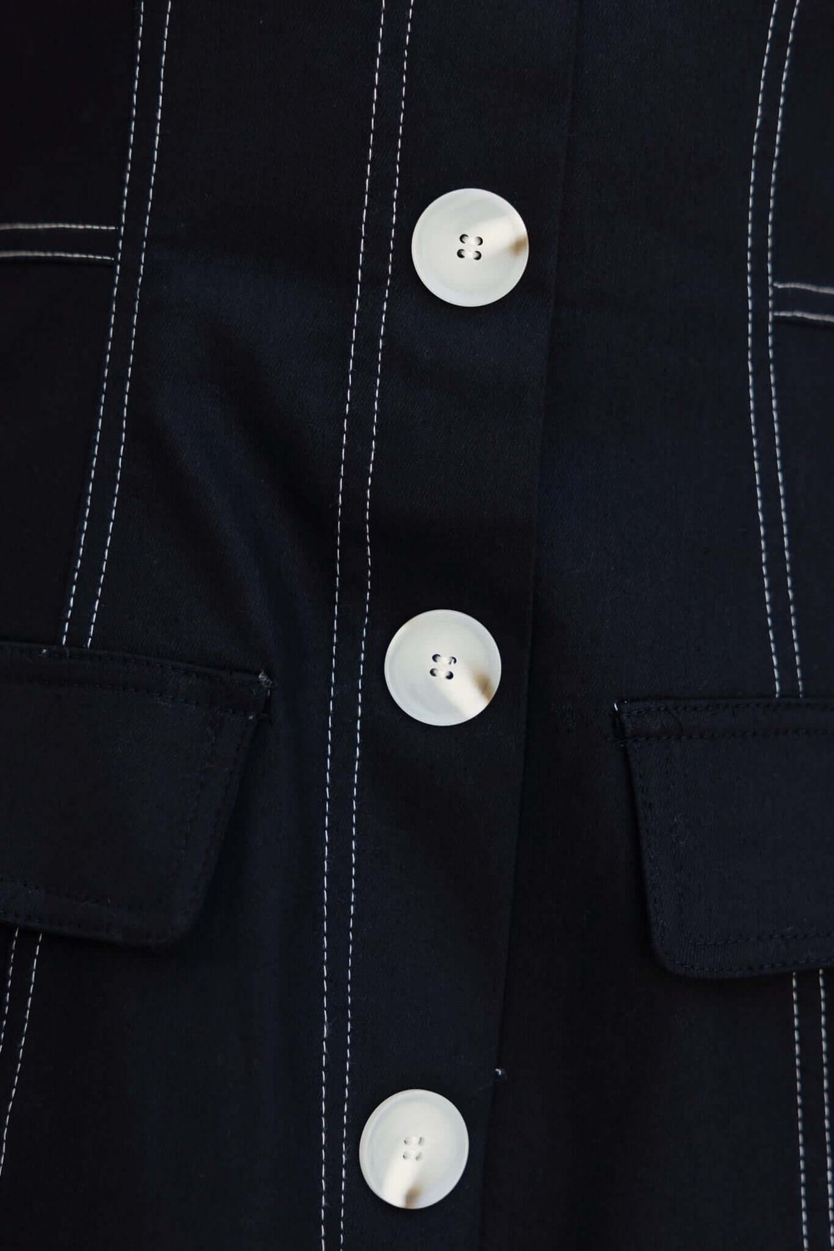 Close-up of the Olean Dress featuring faux buttons and pockets with white stitching on dark fabric.
