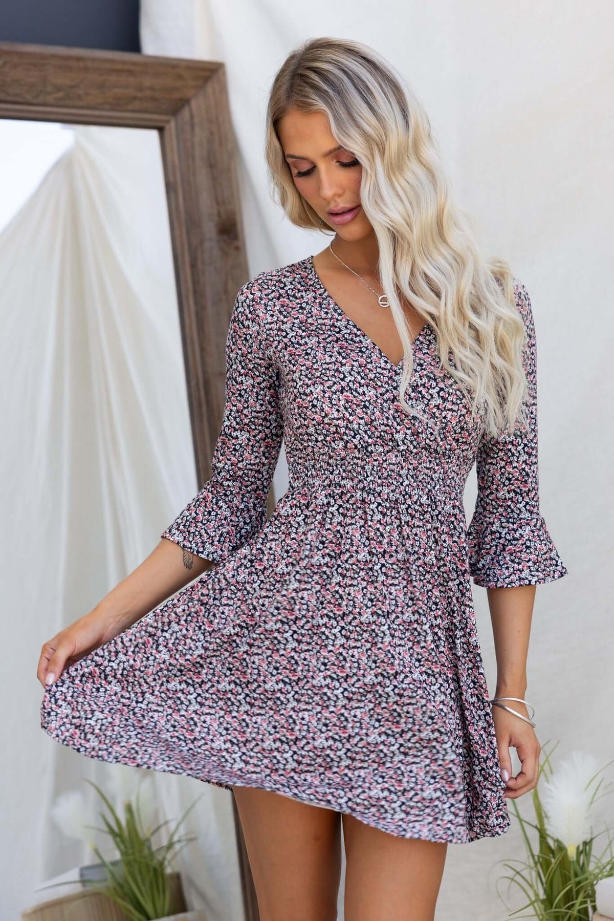 Darien Dress featuring a floral print, button back, elastic waistband, and flared sleeves, modeled by a woman in a bright setting.