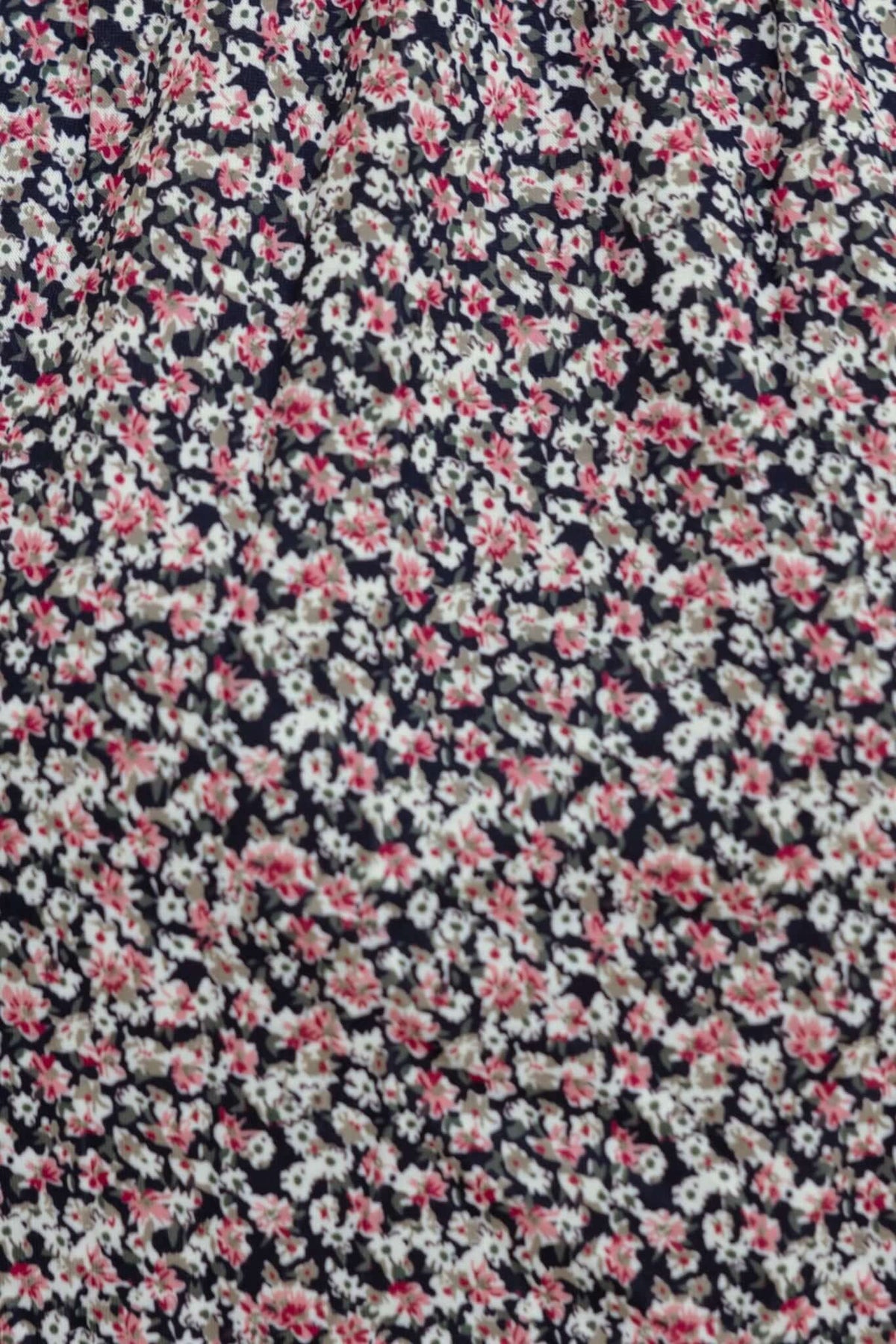 Floral pattern fabric featuring small pink and white flowers on a navy background, ideal for dresses and clothing.