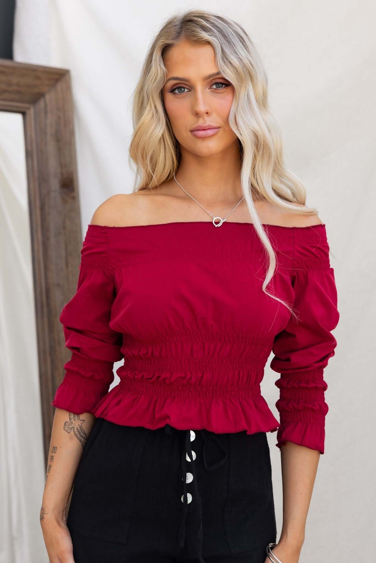 Model wearing a red off-shoulder Jakari Top with elastic detailing, showcasing a stylish and trendy look.