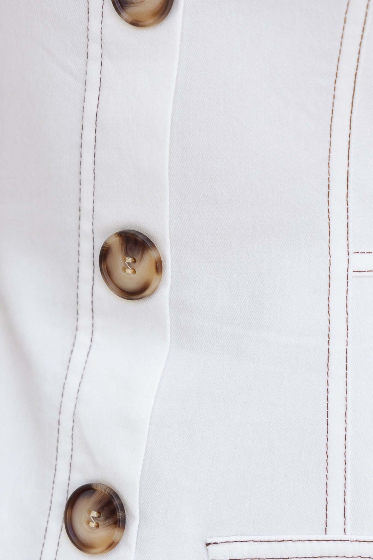 Close-up of Olean Dress featuring faux buttons and detailed stitching on a soft white fabric.