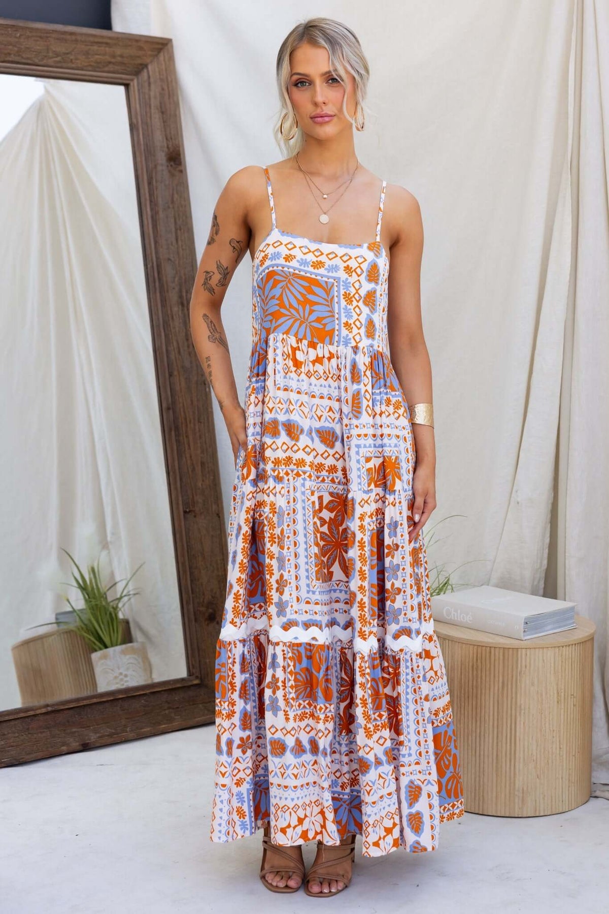 Dapple Maxi Dress featuring adjustable straps, pockets, and a vibrant orange and blue pattern.
