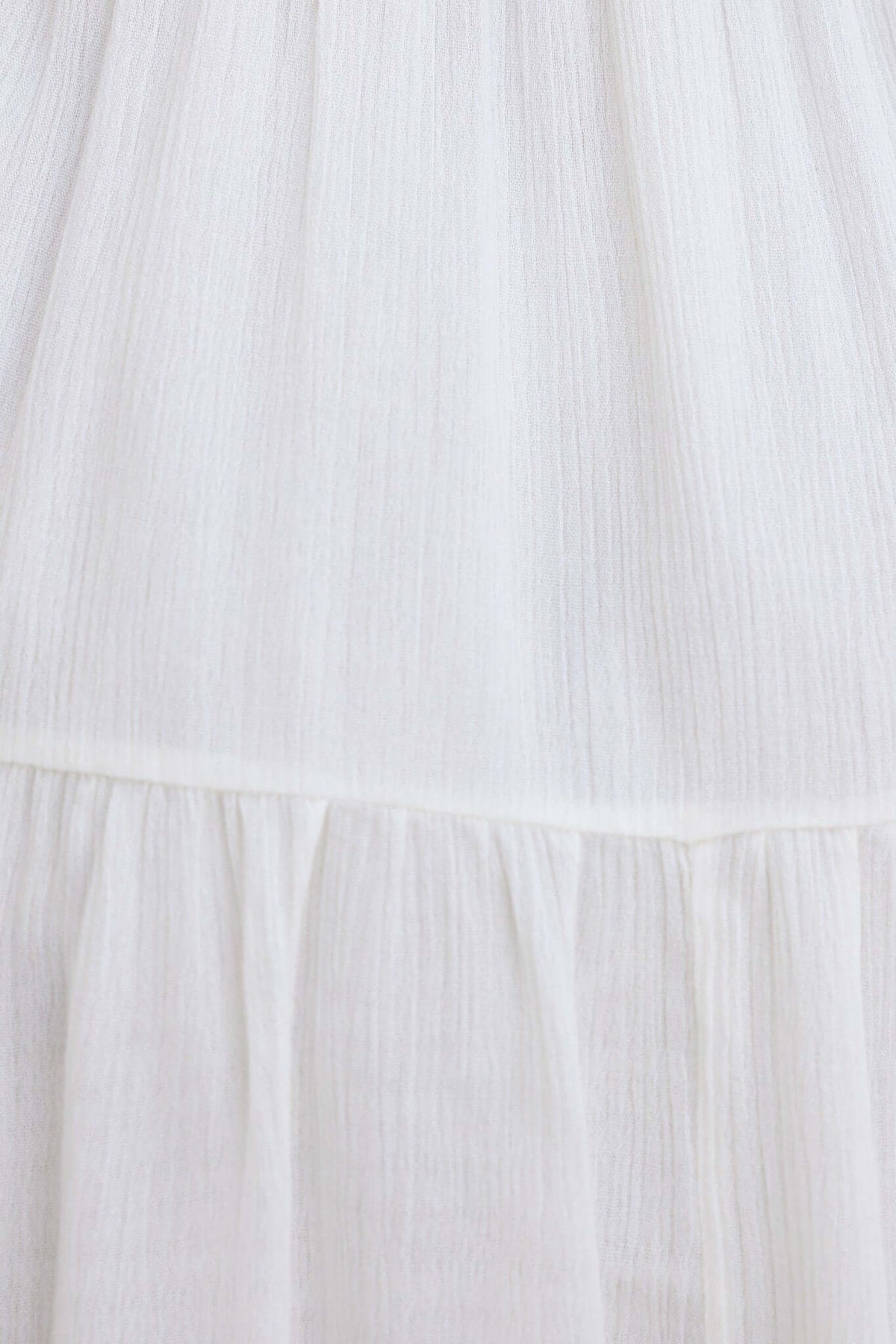 Close-up of the lightweight white fabric of the Harkin Dress, showing its textured layers and elegant design details.