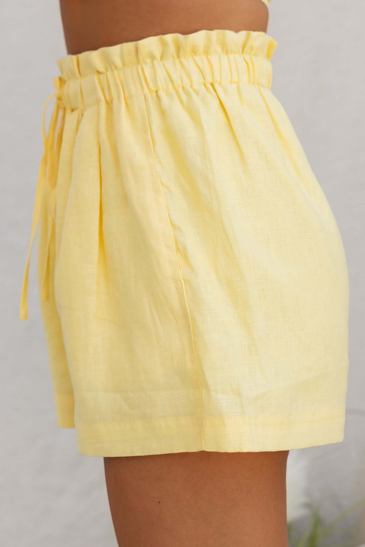 Side view of Orson Shorts, mid-high waist, elastic waistband, in light yellow linen fabric.